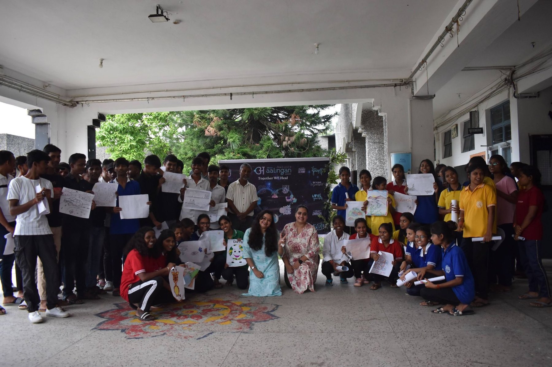 Students and facilitators with their artwork beneath a Together WE Heal banner